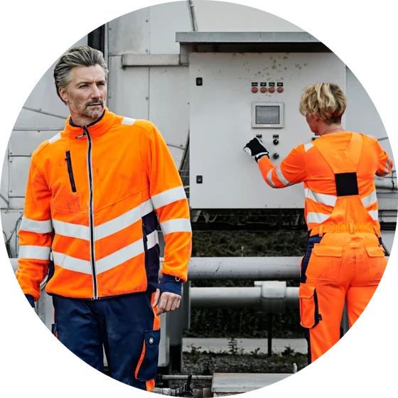 Mitarbeitende in orangefarbener Warnschutz-Arbeitskleidung an einer Anlage